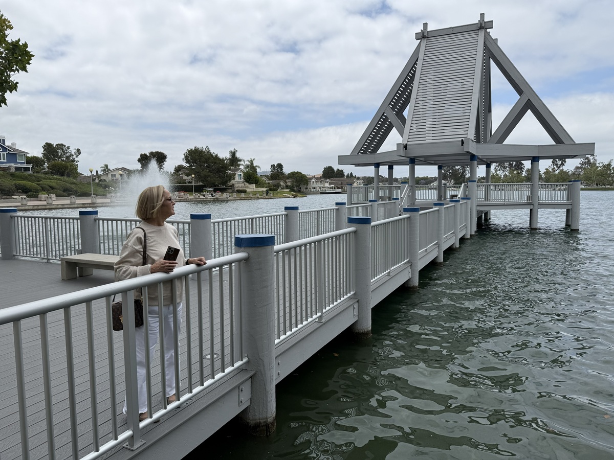 Debbie Sagorin standing at the North Lake gazebo in Woodbridge, Irvine, with the lake and waterfront homes in the background.