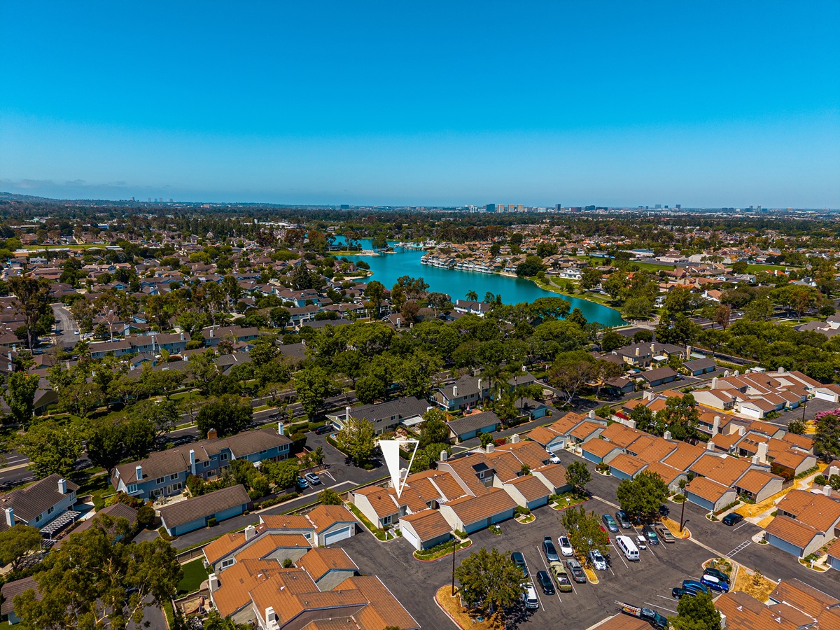 Aerial view of Woodbridge village in Irvine with North Lake, sailboats, and rooflines of surrounding homes on July 31, 2026, illustrating the Woodbridge real estate market update.