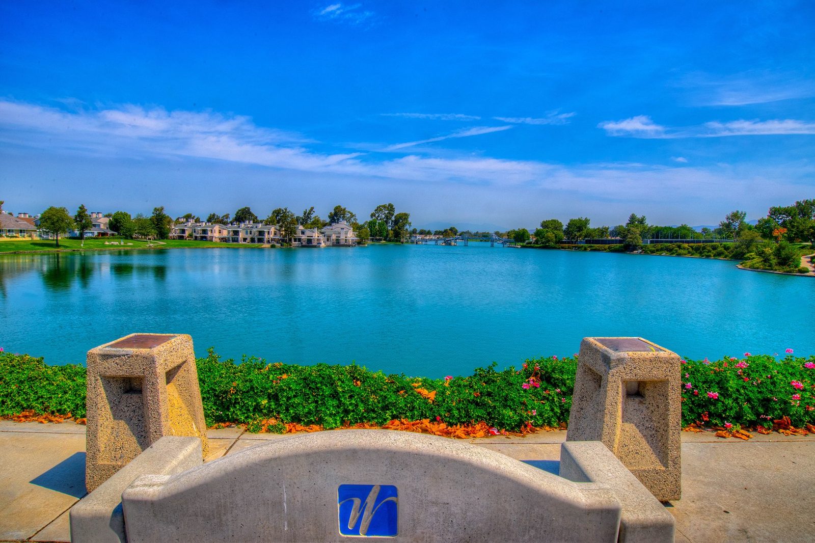 Woodbridge lake in Irvine, California, with lakefront homes across the water and a Woodbridge village emblem in the foreground
